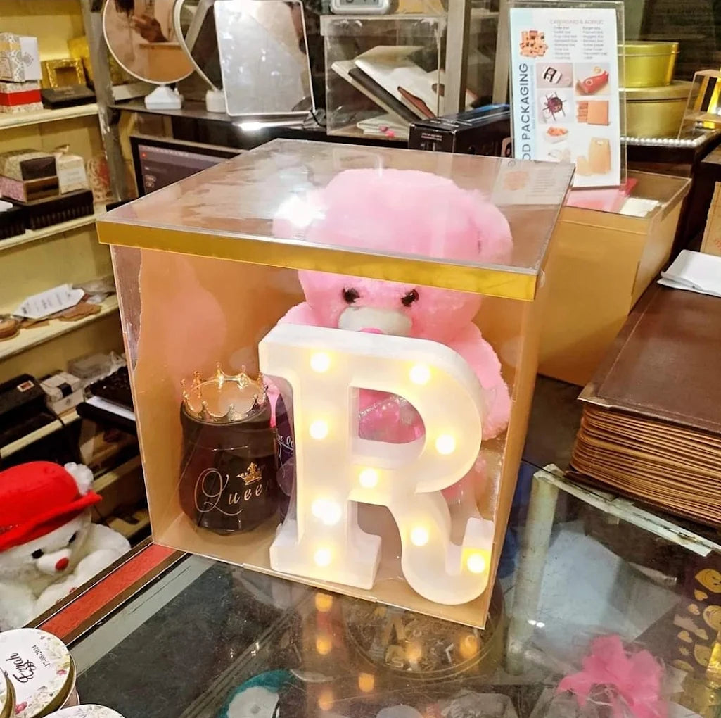 Acrylic gift box with pink teddy bear, illuminated letter R, and decorative candle inside.