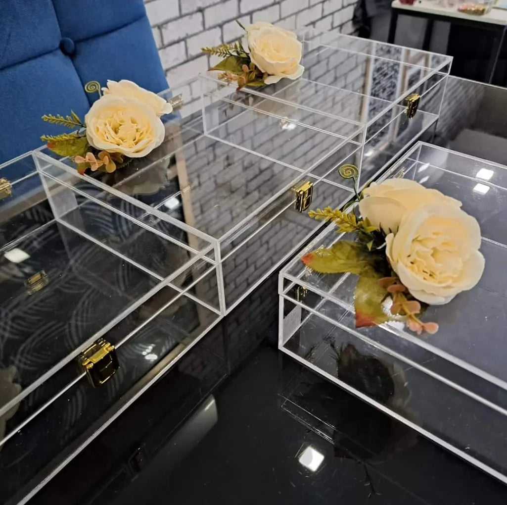 Acrylic wedding gift boxes with artificial flowers and gold clasps on a table